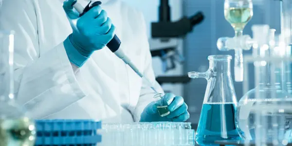 A person in a lab coat holds a test tube, focused on their work in a laboratory setting, surrounded by scientific equipment.