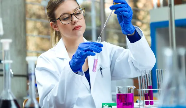 A woman in a lab coat holds a test tube, focused on her work in a laboratory setting, surrounded by scientific equipment.