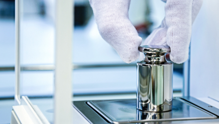 A person wearing white gloves holds a shiny metal cylinder, showcasing careful handling and attention to detail.