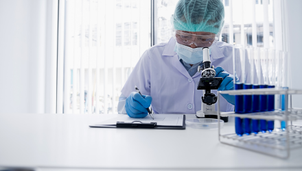 A person in a lab coat writes on a clipboard, focused on their task in a laboratory setting.