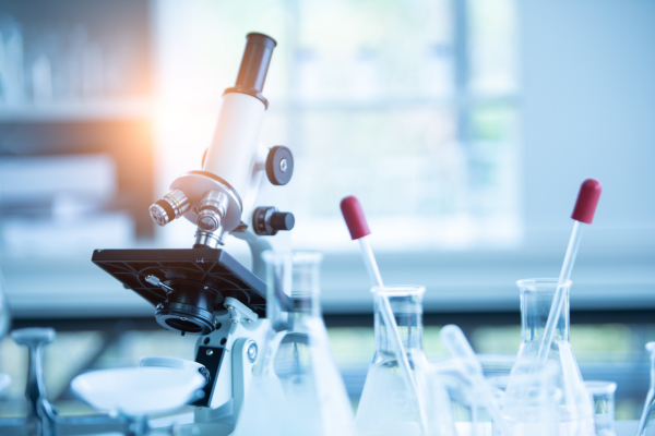 A microscope and a beaker are placed on a table, indicating a laboratory setting for scientific experiments or observations.